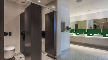 A modern restroom with dark wooden doors, a white toilet, and a counter with sinks and a mirror.