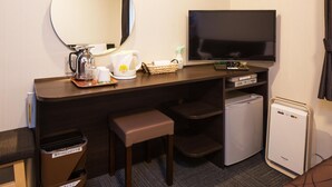 Ein Hotelzimmer mit Schreibtisch, Fernseher, kleinem Kühlschrank, Mülleimer und Sitzbank.