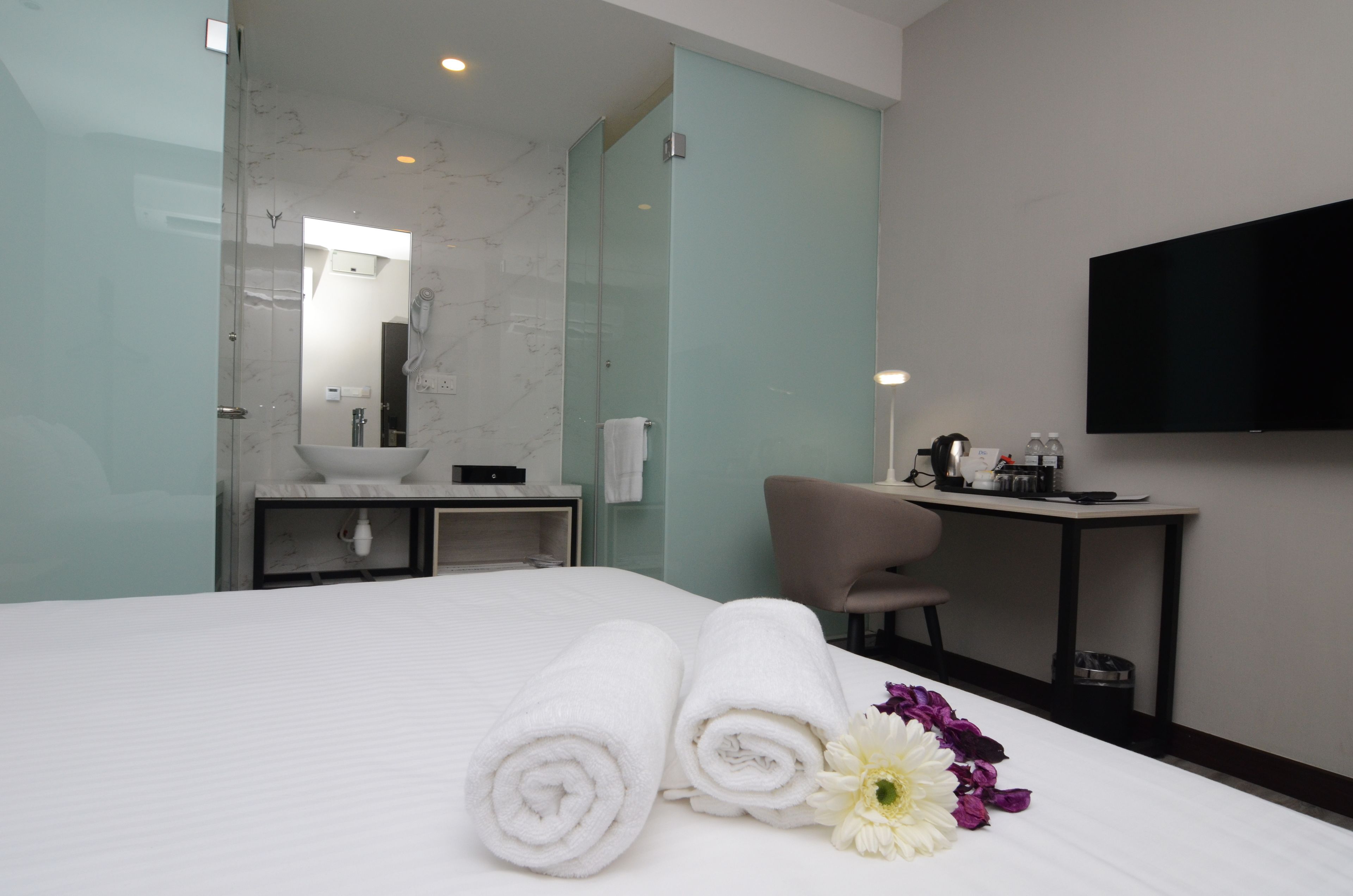 Habitación de hotel con cama, baño con lavamanos y espejo, escritorio con silla y televisor en la pared.