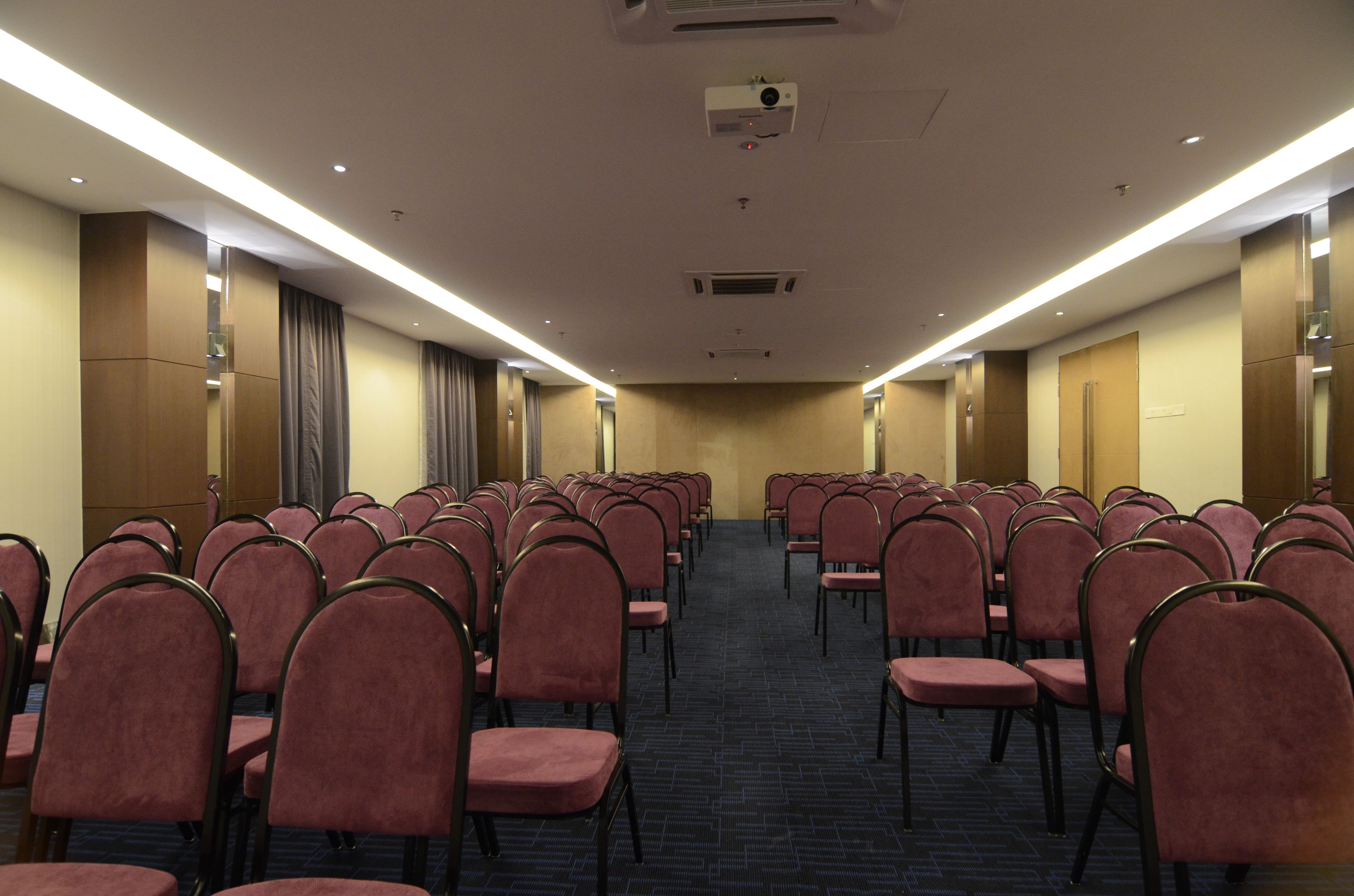 Une salle de conférence avec des rangées de chaises, un sol recouvert de moquette et un projecteur au plafond.