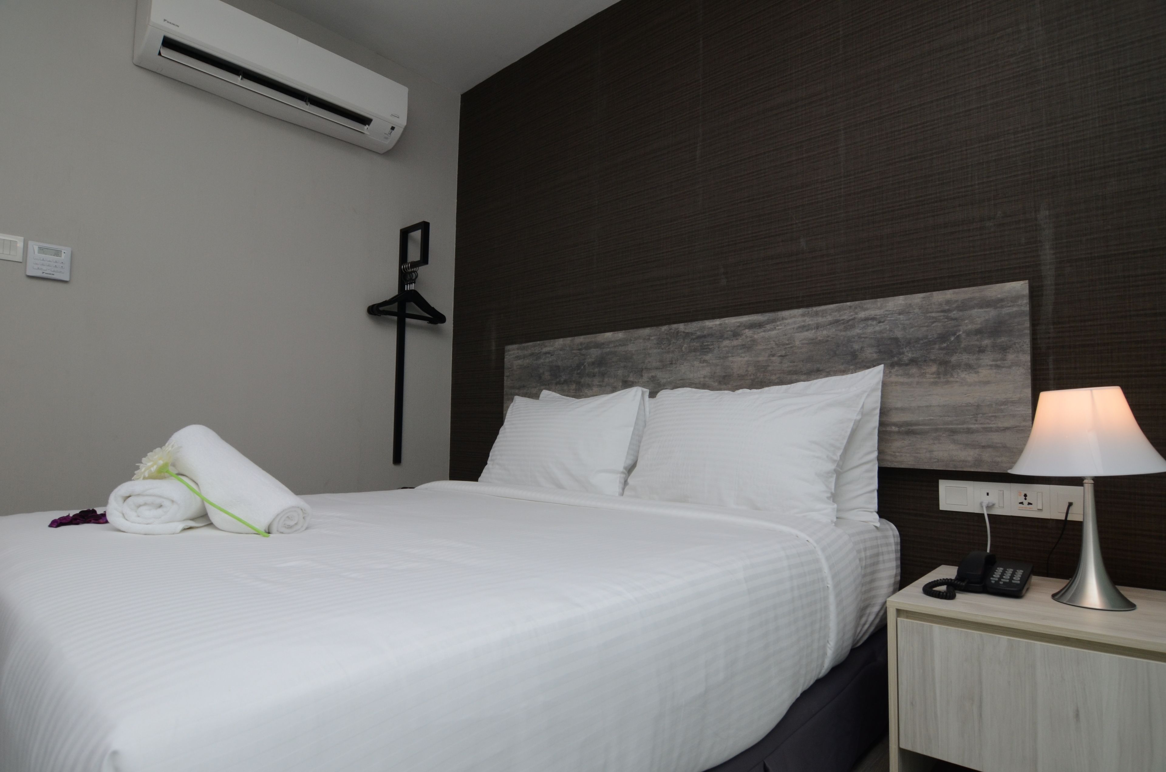 A neatly made bed with white linens, a bedside lamp, a phone, and a wall-mounted air conditioner.