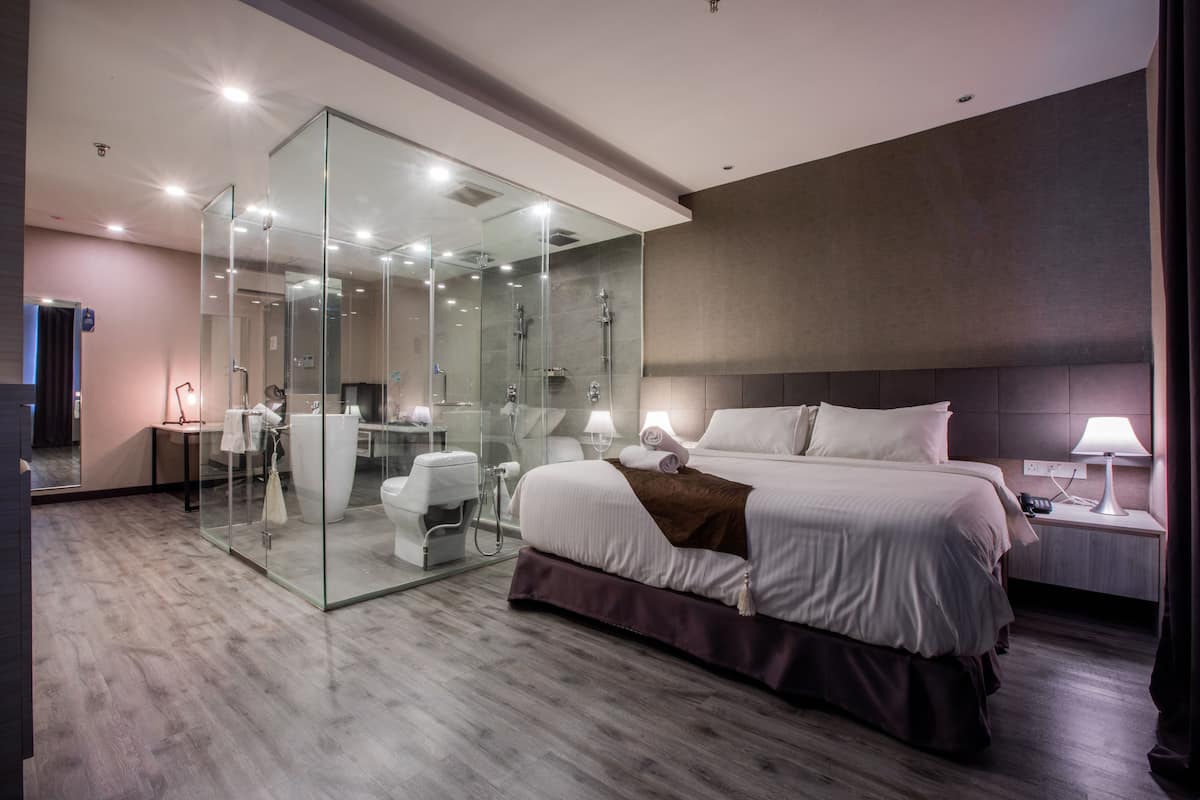 Una habitación de hotel moderna con ducha de vidrio, una cama grande, una mesita de noche y una lámpara.