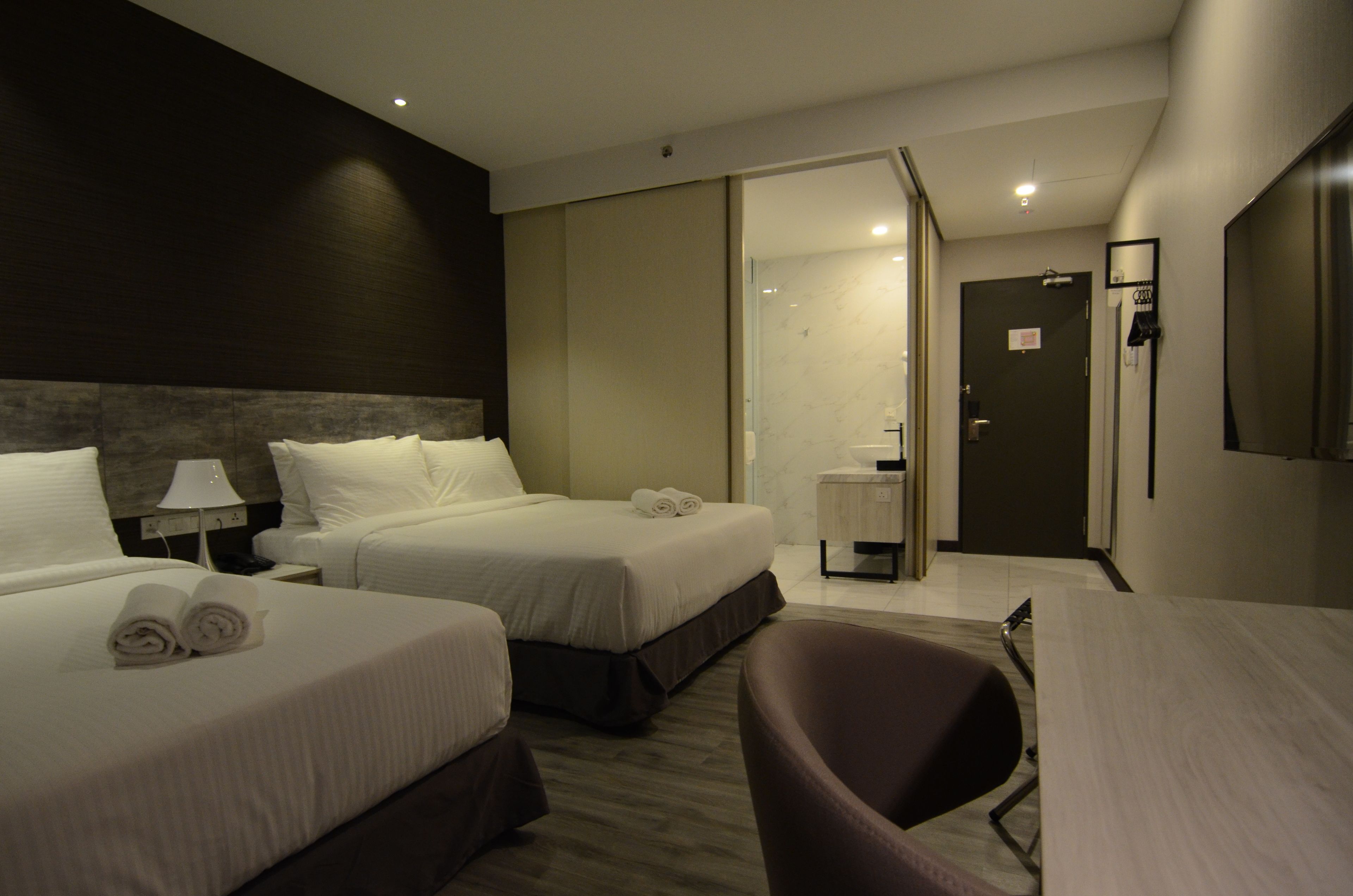 Hotelkamer met twee bedden, een bureau, een stoel, een spiegel en een badkamer zichtbaar door een open deur.
