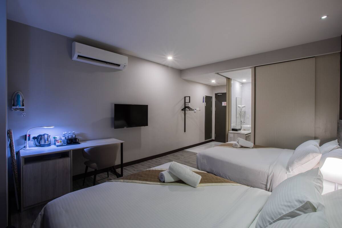 Habitación de hotel con dos camas, un escritorio, un televisor de pantalla plana, un espejo y un equipo de aire acondicionado.