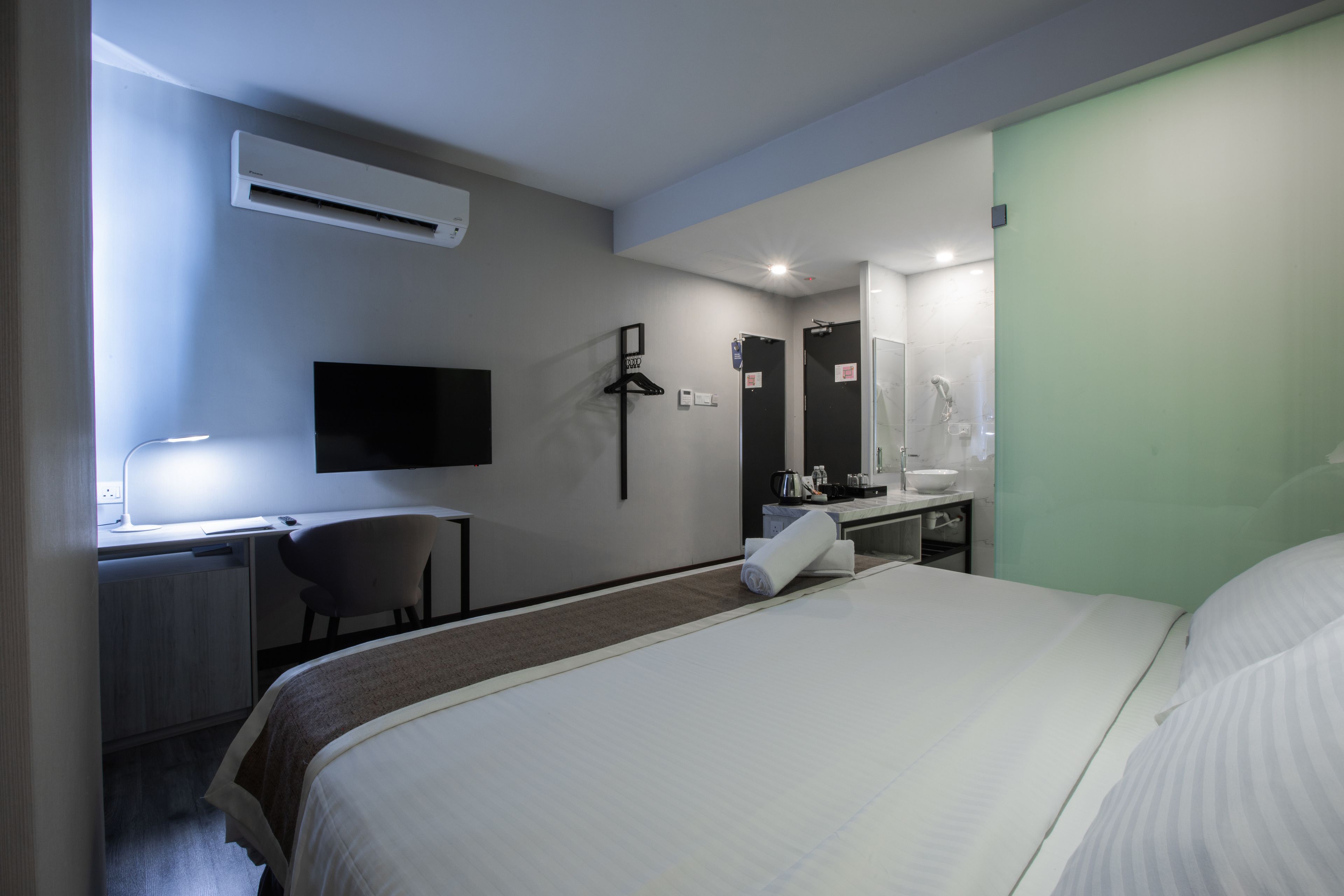 A hotel room with a bed, desk, chair, and a bathroom with a sink and mirror.