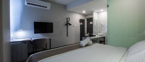 A hotel room with a bed, desk, chair, and a bathroom with a sink and mirror.