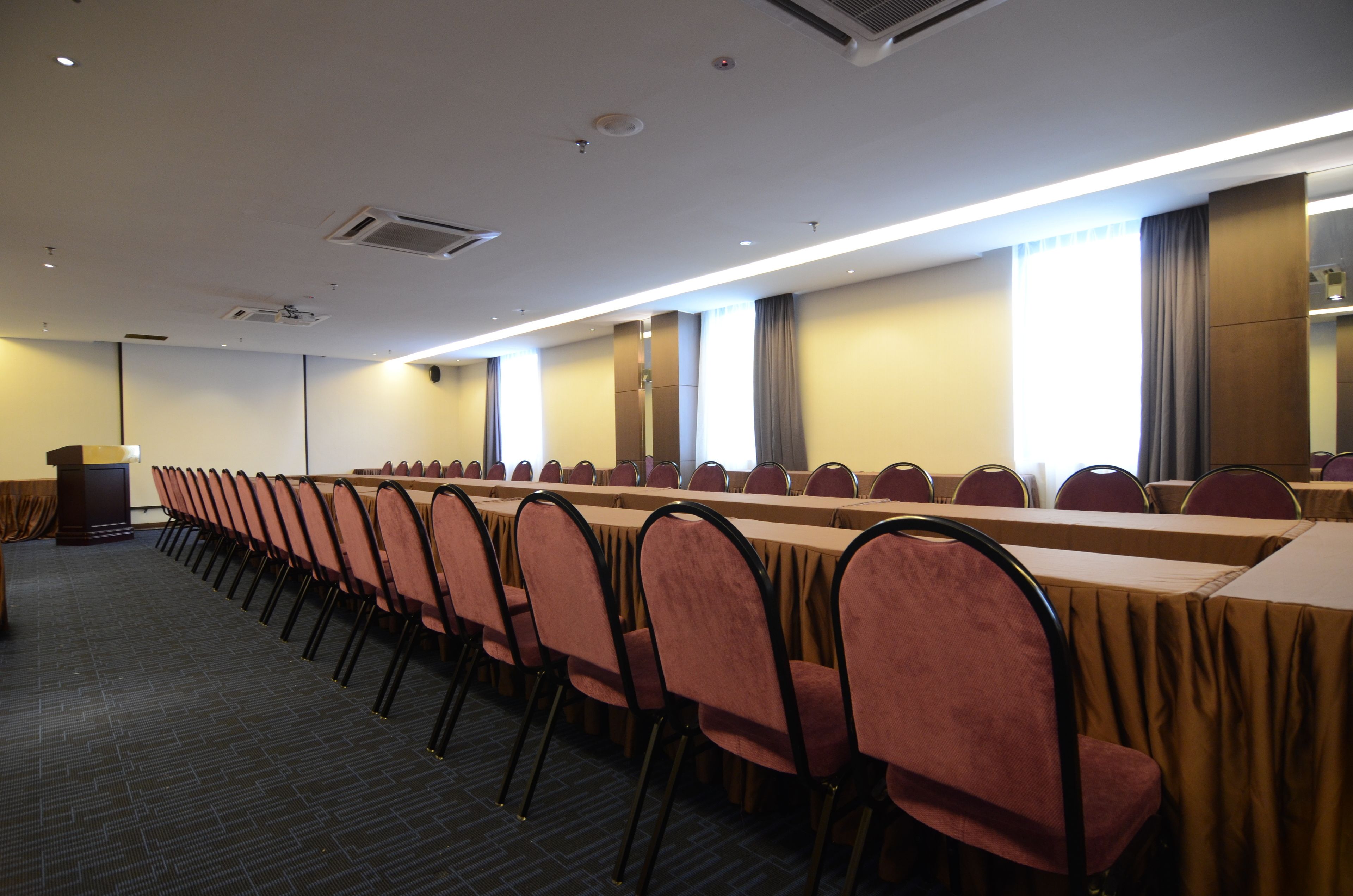 A conference room with a long table and chairs, a podium, and large windows with curtains.