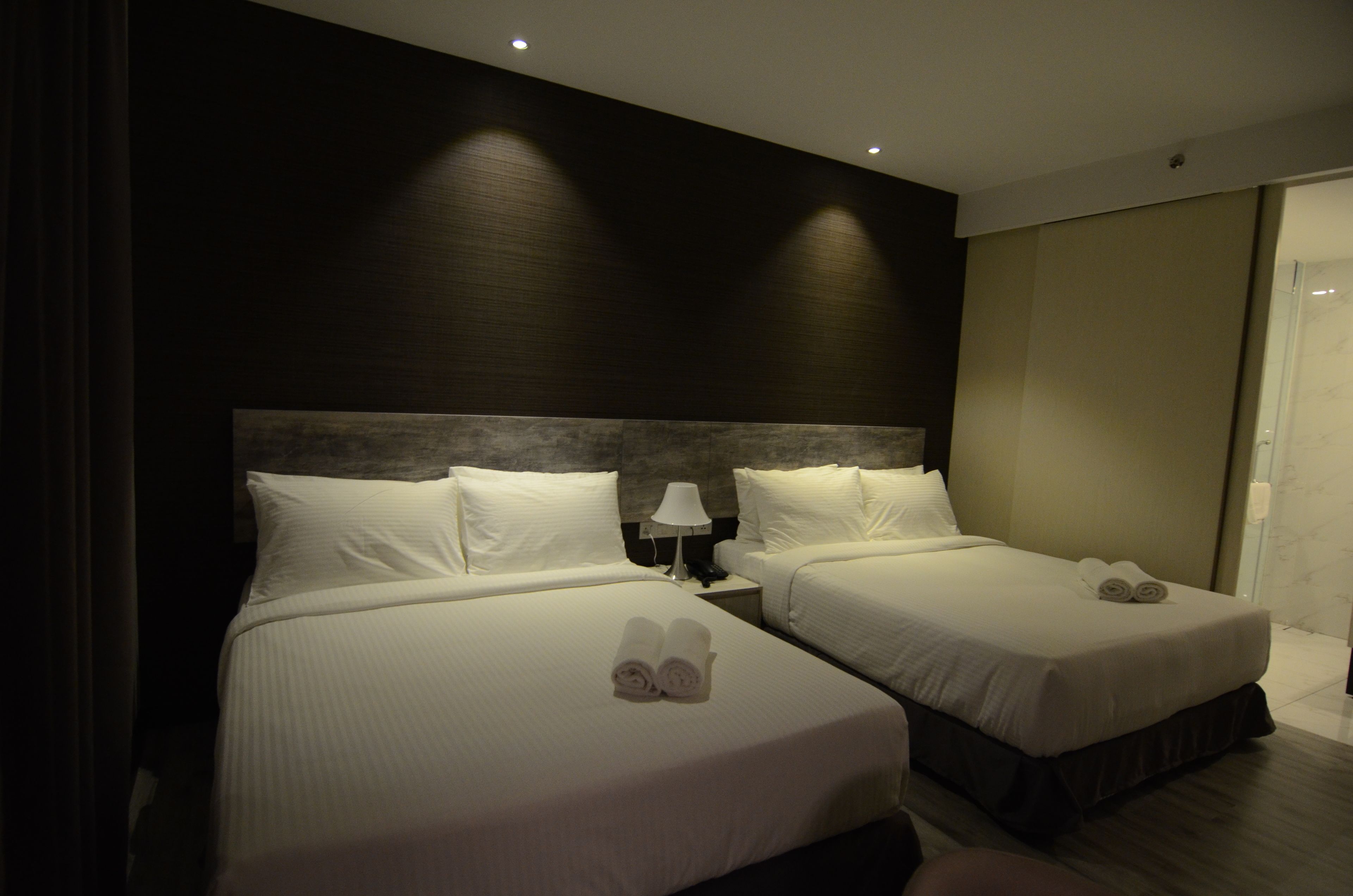 Quarto de hotel com duas camas, uma mesa de cabeceira com abajur e uma janela grande.