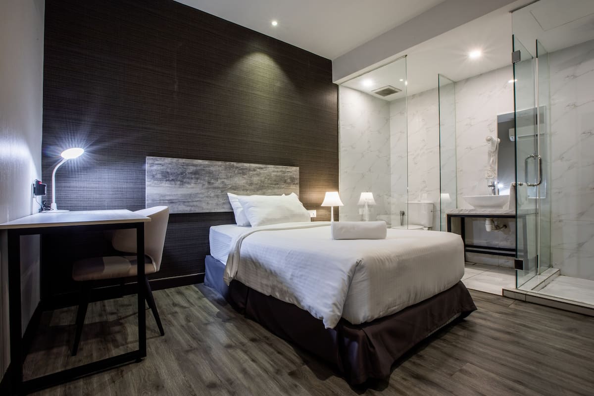 Una habitación de hotel moderna con cama, escritorio y zona de ducha con paredes de vidrio.