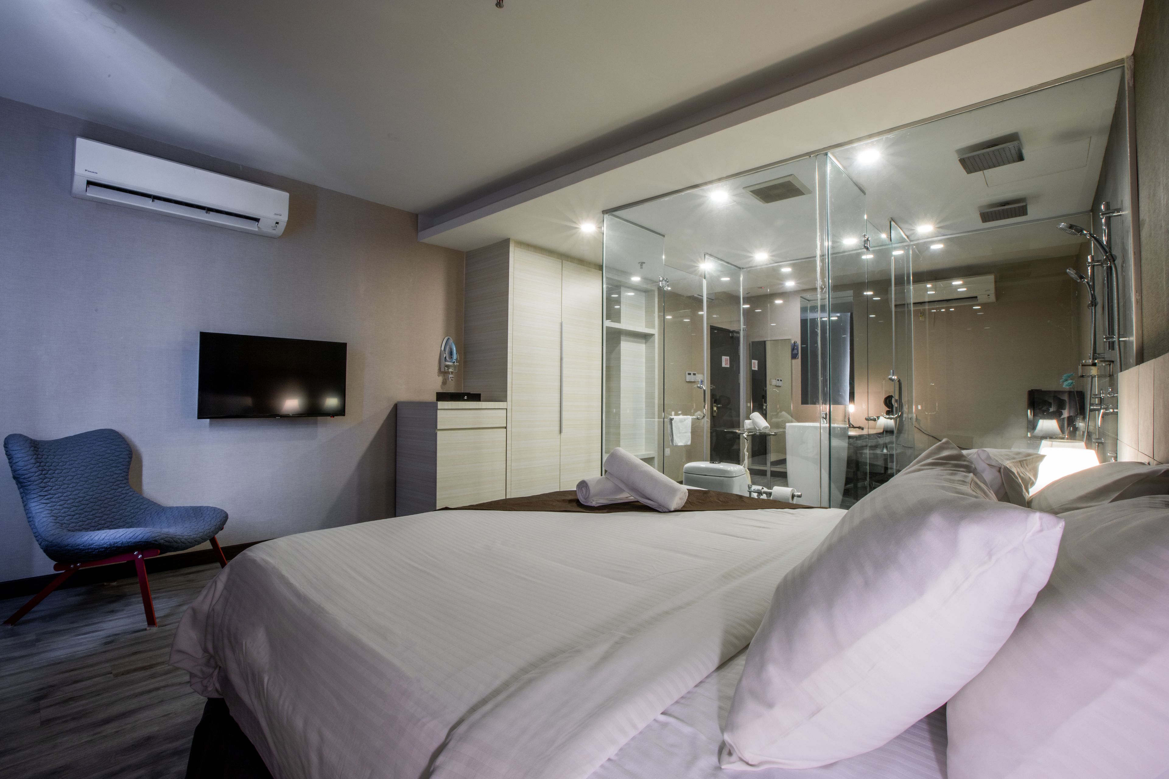 A hotel room with a large bed, a flat-screen TV, a chair, and a glass shower area.