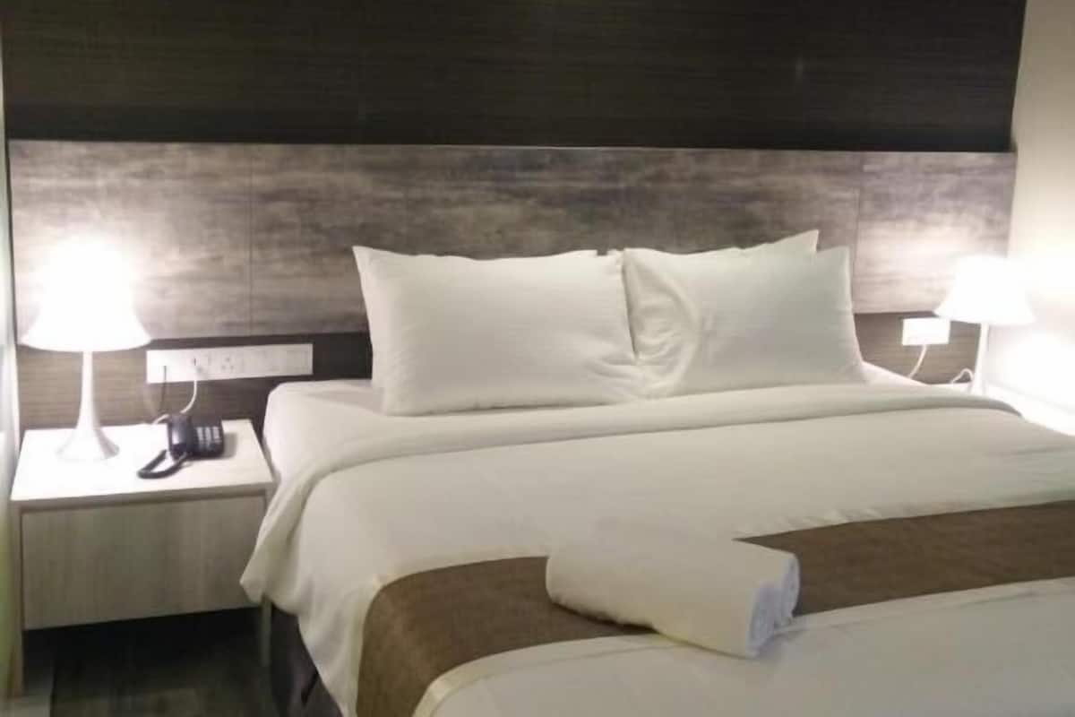Una habitación de hotel con una cama grande, dos mesitas de noche con lámparas y un cabecero oscuro.