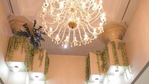 Un hall d’entrée agrémenté d’un lustre, de colonnes, d’un comptoir de réception et de plantes suspendues.