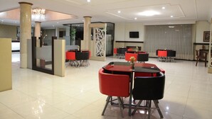 Un hall d’hôtel moderne comprenant un comptoir d’accueil, plusieurs tables à manger avec des chaises et un pilier décoratif.