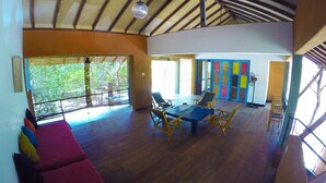 A spacious room with a high ceiling, a large wooden table, and several chairs. There is a window with a view of greenery outside. - Wapi Bungalowi Yala (Thissamaharama)