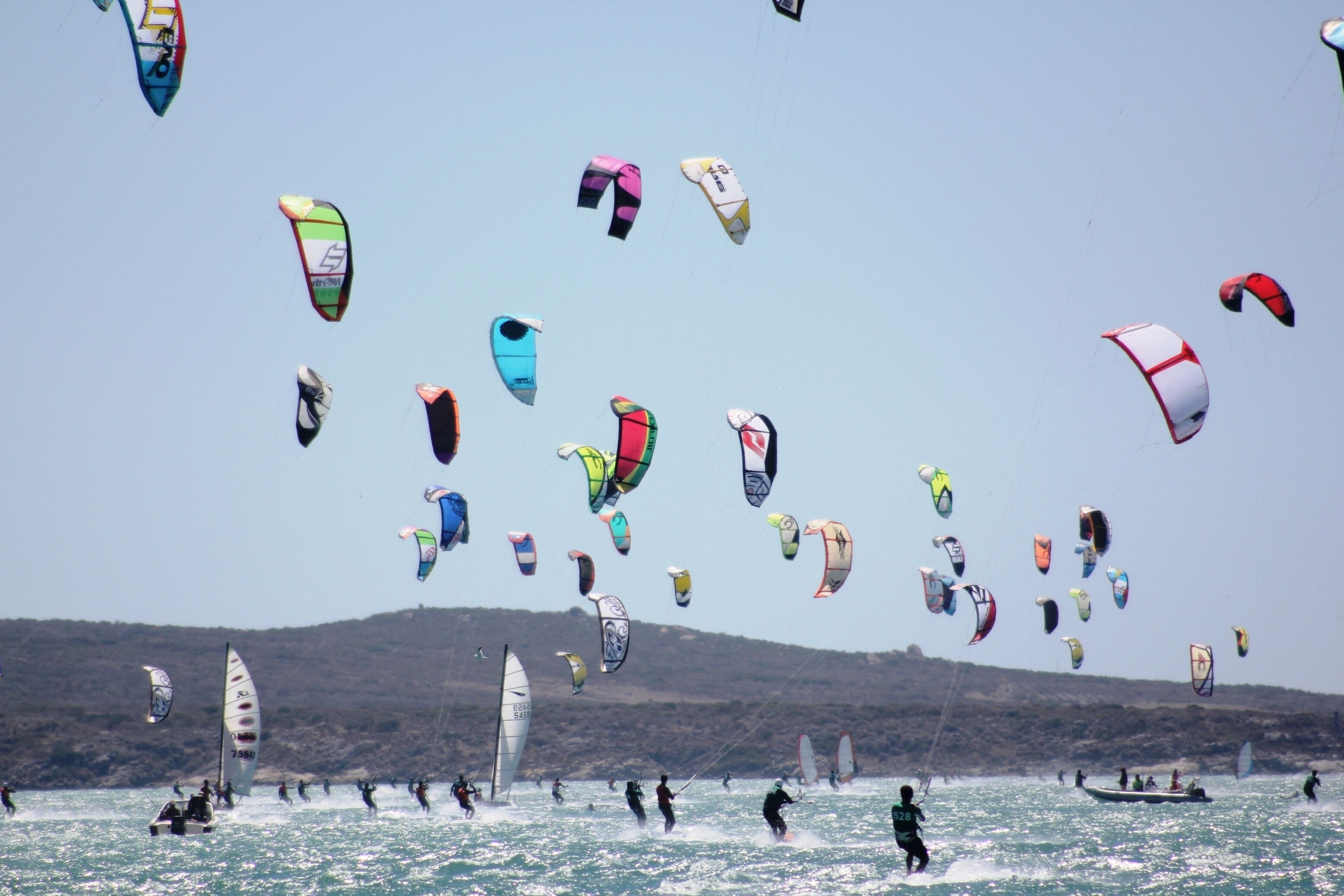 A group of people windsurfing and parasailing on a body of water with hills in the background.