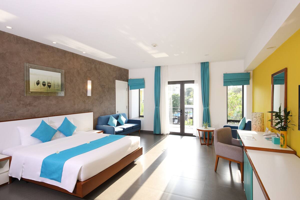 A modern hotel room with a large bed, a desk, and a balcony.