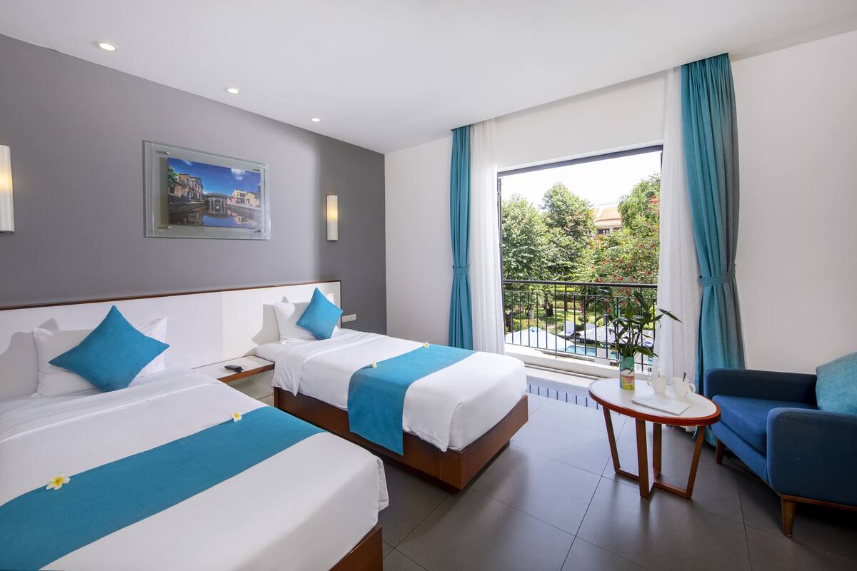 A hotel room with two beds, a balcony with a view, a small table, and a blue sofa.