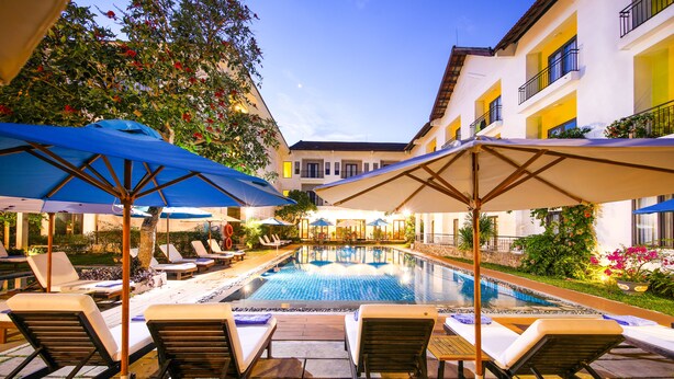 A poolside area with lounge chairs and umbrellas, surrounded by buildings with balconies. - ÊMM Hotel Hoi An (Da Nang)
