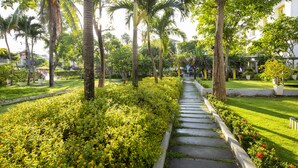A pathway lined with lush greenery and palm trees, leading to a building with a yellow door. - ÊMM Hotel Hoi An (Da Nang)