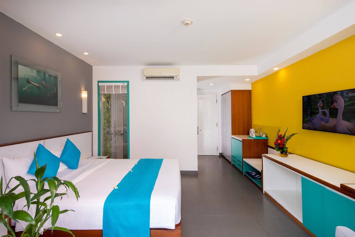 A hotel room with a bed, a desk, a TV, and a door leading to a bathroom.
