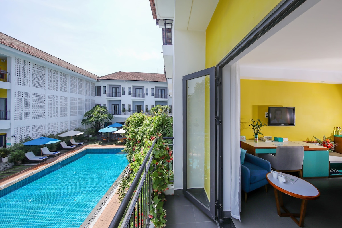 A hotel room with a balcony overlooking a swimming pool, a dining area, and a TV.