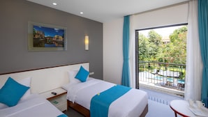 A hotel room with two beds, a painting on the wall, a balcony with a pool view, and a table with a cup and a notebook. - ÊMM Hotel Hoi An (Da Nang)