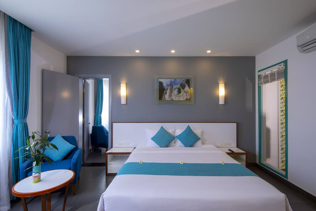 A hotel room with a bed, a desk, a chair, and a potted plant.