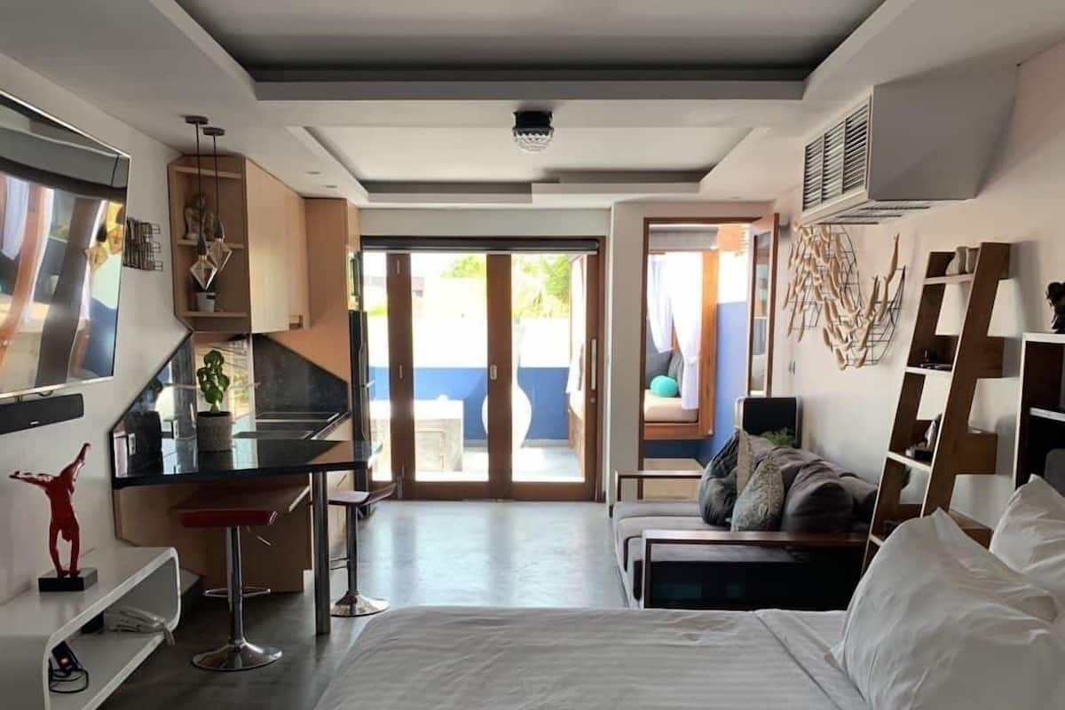 A modern hotel room with a large bed, a desk, a TV, and a balcony with a view.