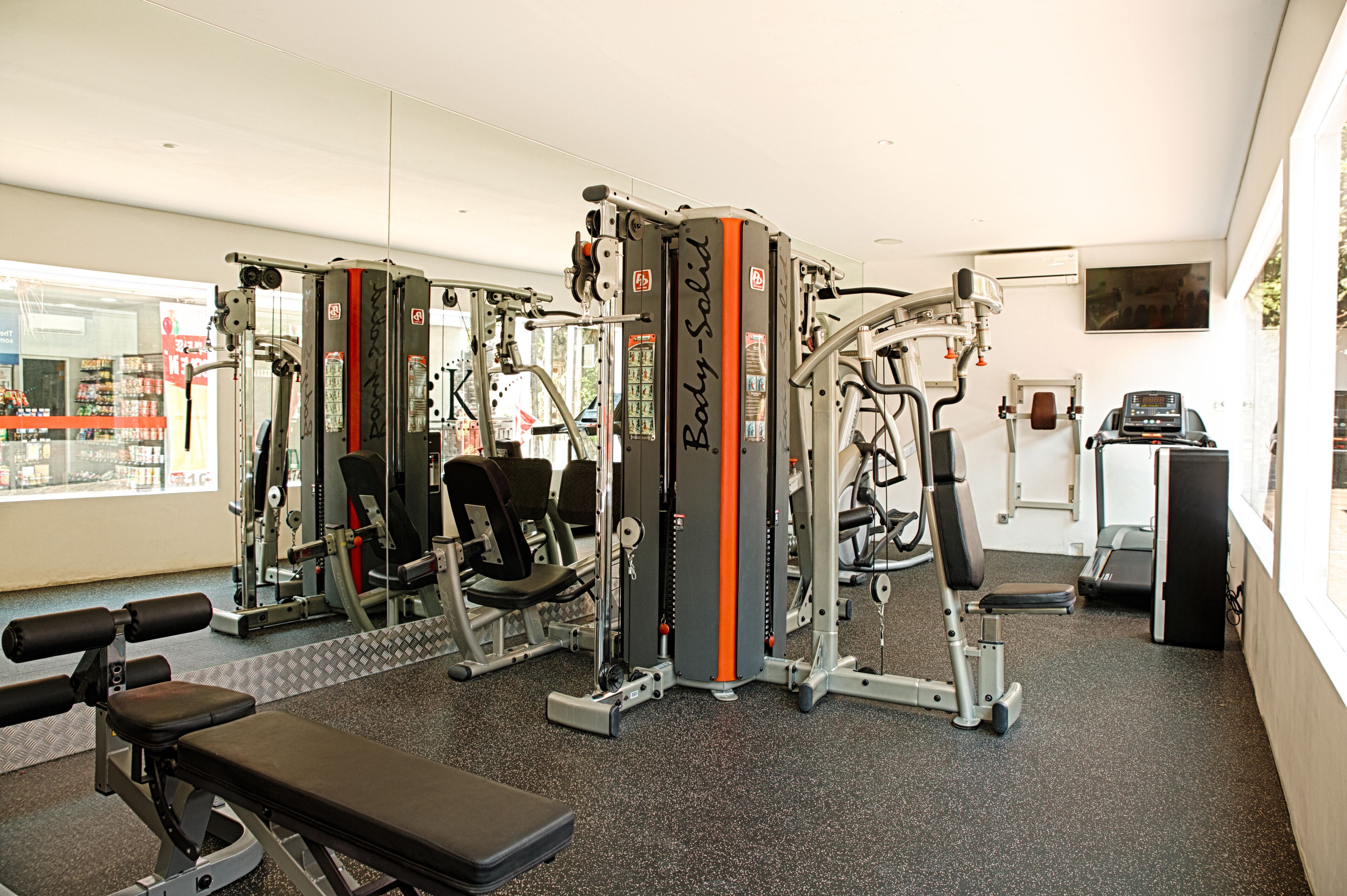 Un gimnasio con diferentes máquinas de ejercicio, una banca y una cinta de correr.