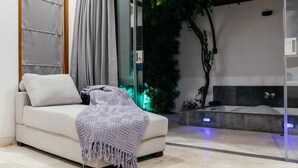 A modern spa room with a white sofa, a large window with curtains, a bathtub, and a green plant wall. - Kamil Villas (Seminyak)