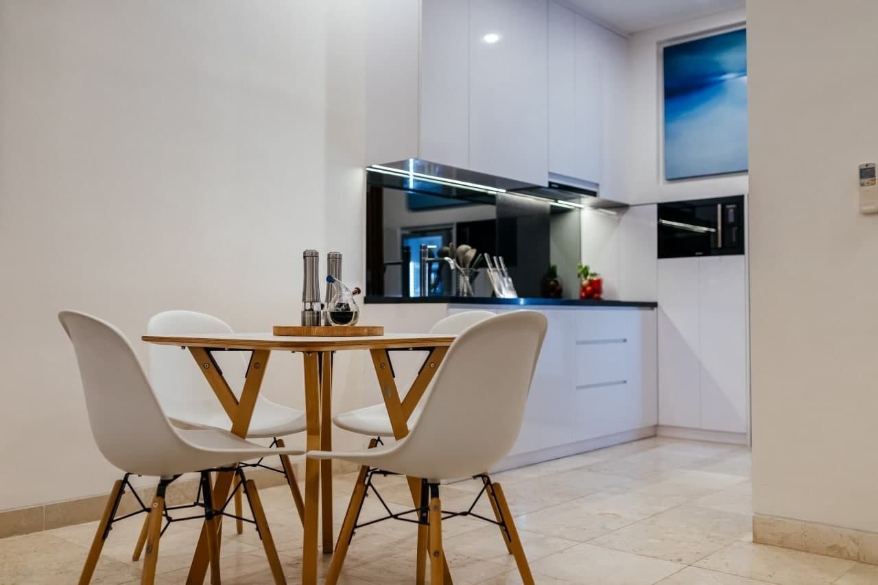 A modern kitchen with white cabinets, a black countertop, and a dining area with a wooden table and white chairs.