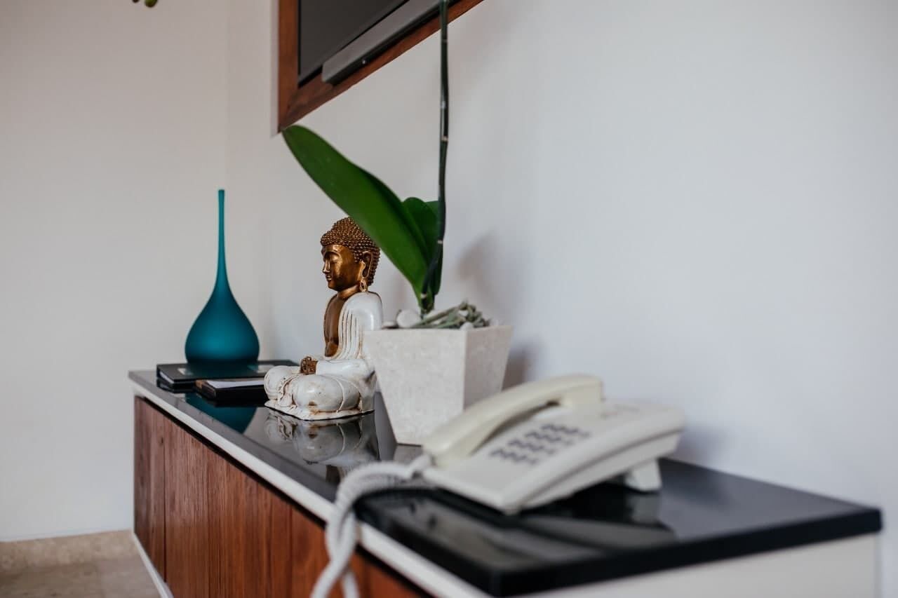 A desk with a telephone, a blue vase, a Buddha statue, and a potted plant.