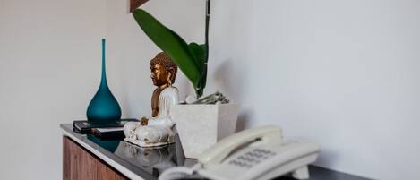 A desk with a telephone, a blue vase, a Buddha statue, and a potted plant.