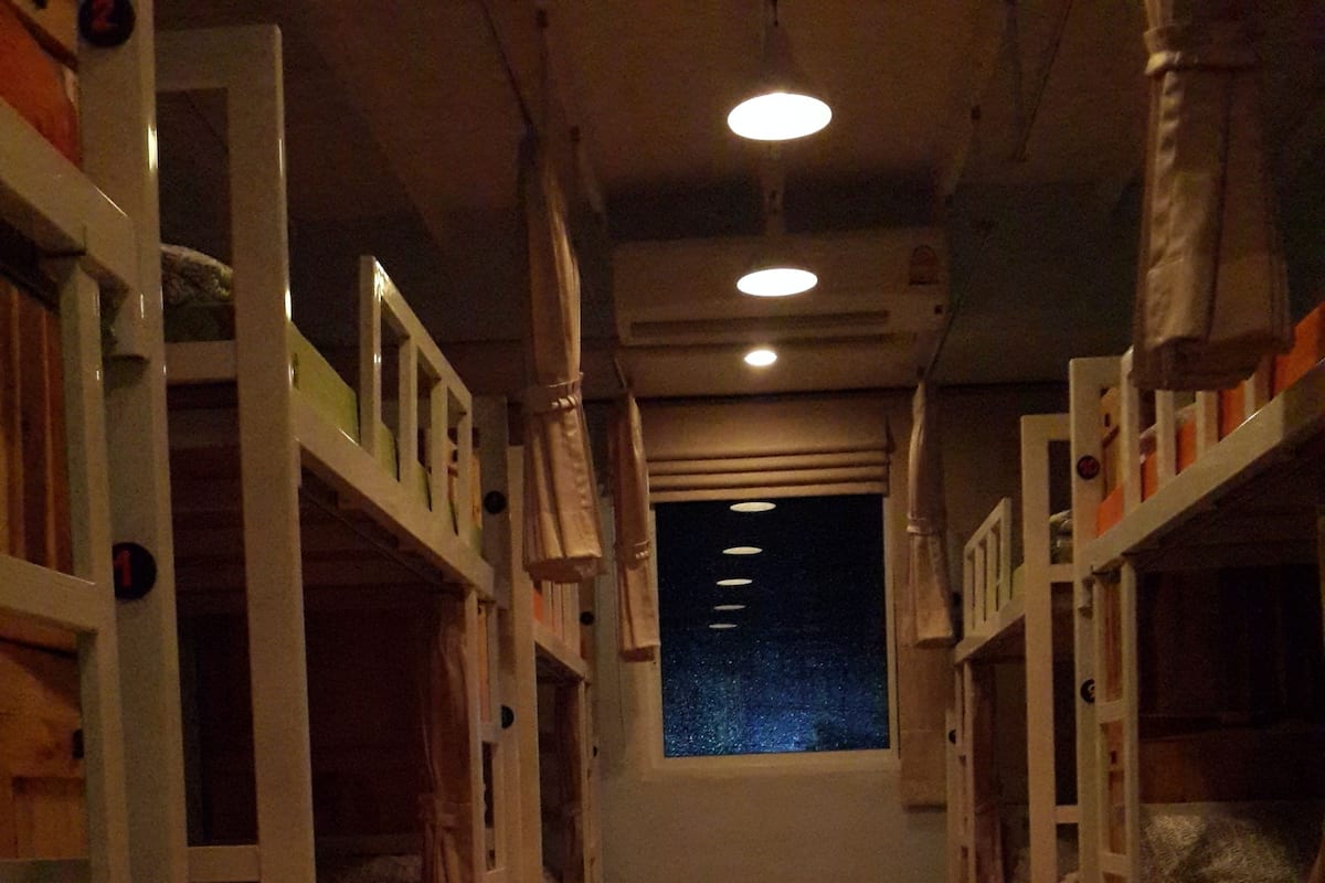 A dormitory room with bunk beds, a window with a view of the night sky, and a tiled floor.