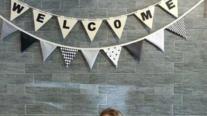 A person seated at a table with a breakfast setting, a 'WELCOME' banner above, and a brick wall background. - Eat - Ting Cafe and Hostel (Bangkok)