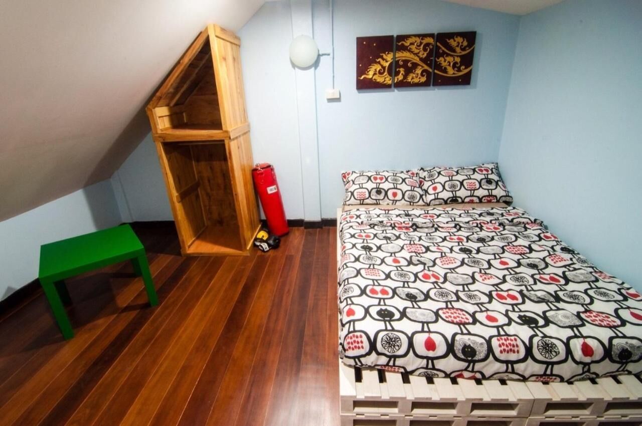 Un dormitorio con una cama nido de madera, un banco verde, un edredón estampado y decoración mural.