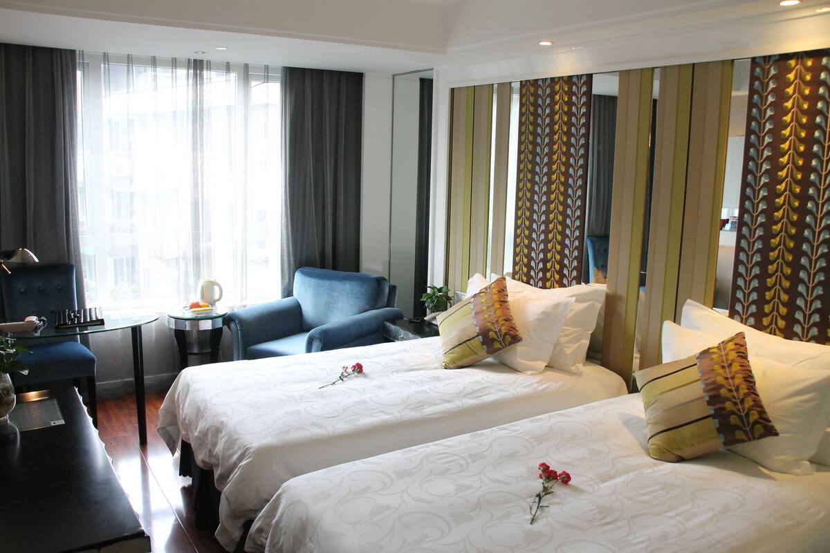 Habitación de hotel con dos camas, un escritorio, una silla y un espejo grande.