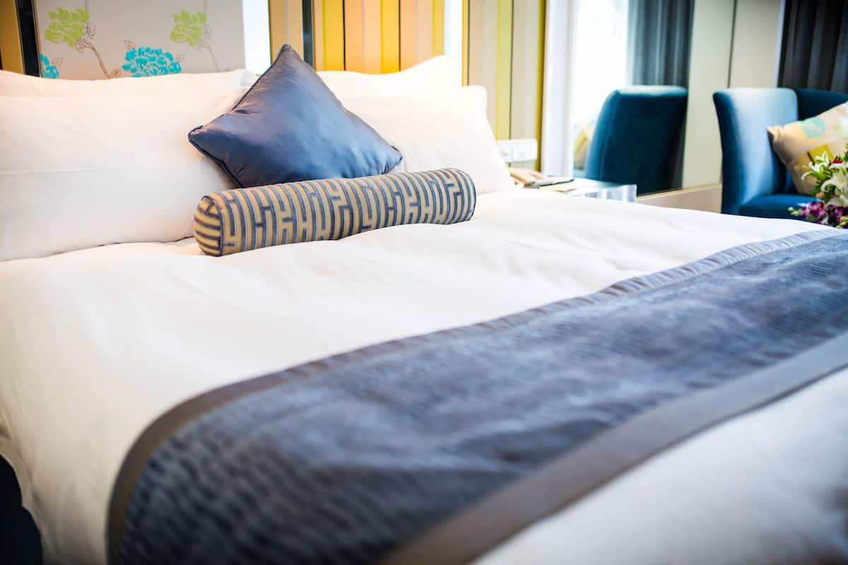 Una cama bien hecha con un almohadón a rayas, un almohadón azul y una manta gris.