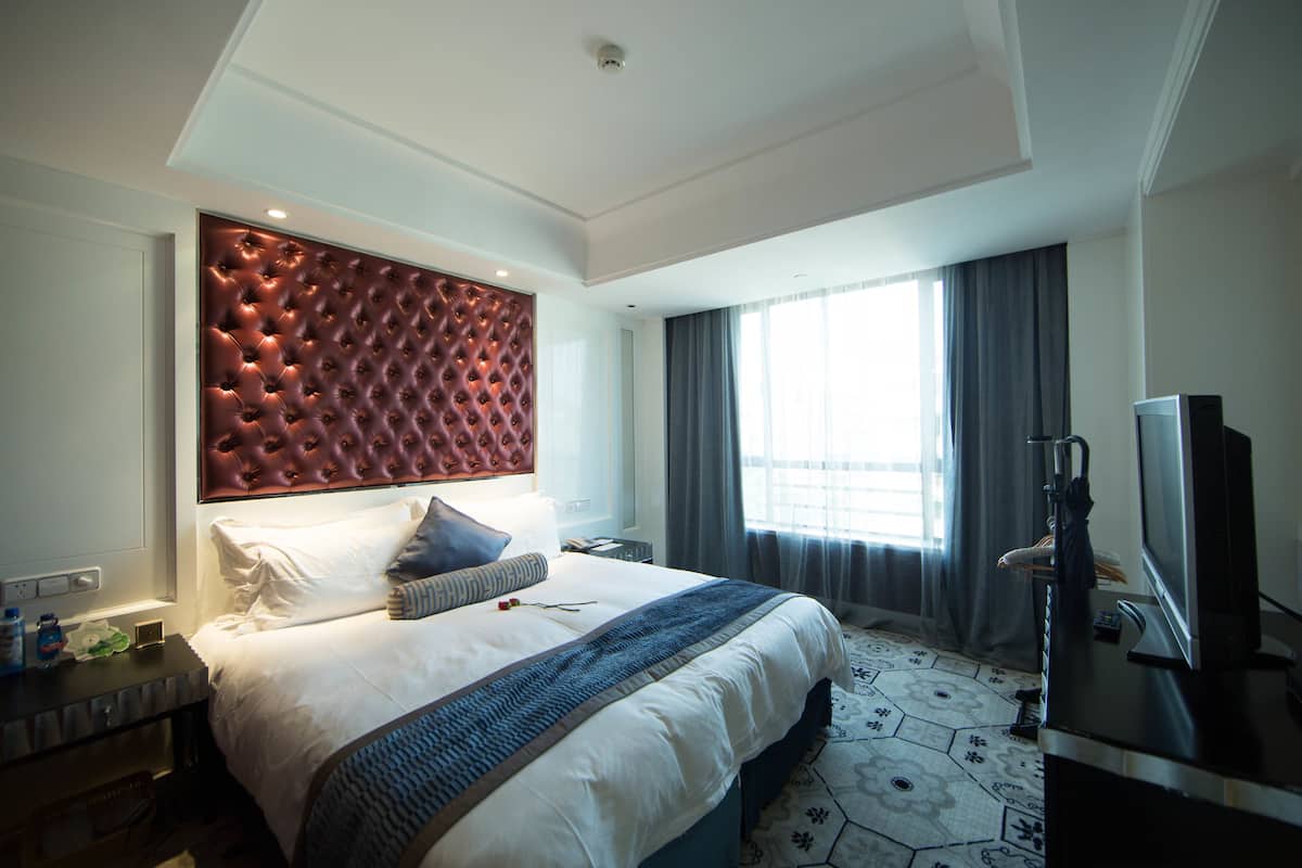 Una habitación de hotel moderna con una cama grande, televisor y ventana con cortinas.