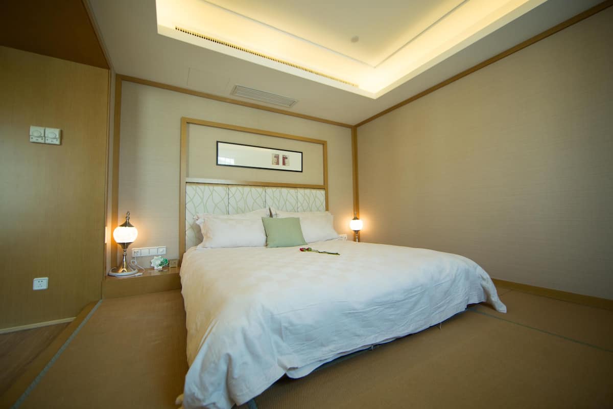Una habitación de hotel con una cama grande, dos lámparas de noche, una mesita de noche y un cuadro en la pared.