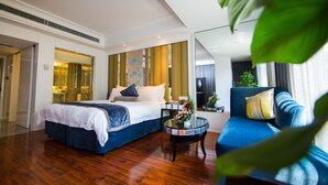A modern hotel room with a large bed, a blue sofa, a small table with a vase, and a large window.