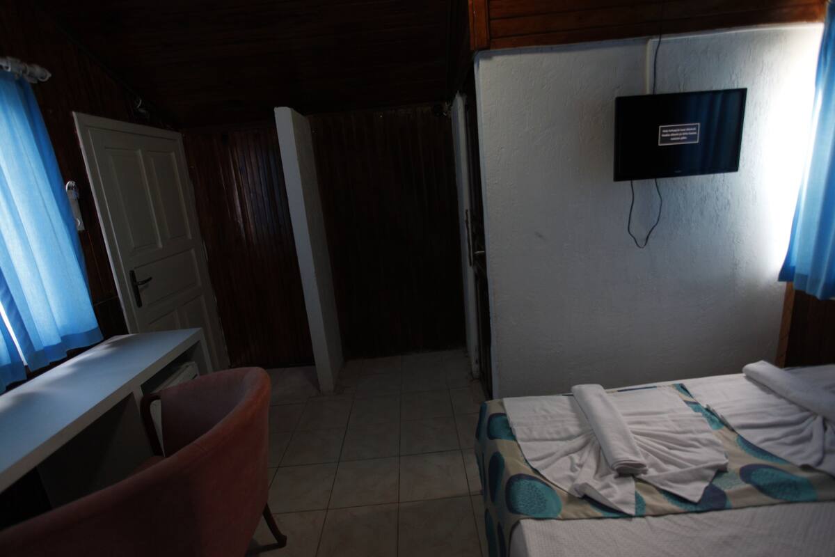 Una habitación pequeña y tenuemente iluminada con una cama, un escritorio y un televisor montado en la pared.
