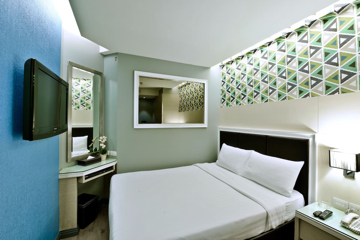 Una habitación de hotel con cama, escritorio, espejo, televisión y pared con diseño.
