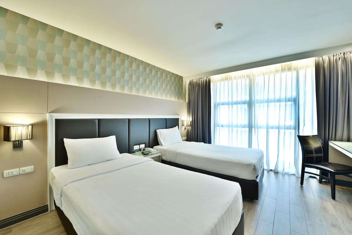Habitación de hotel con dos camas, un escritorio, una silla y un ventanal con cortinas.