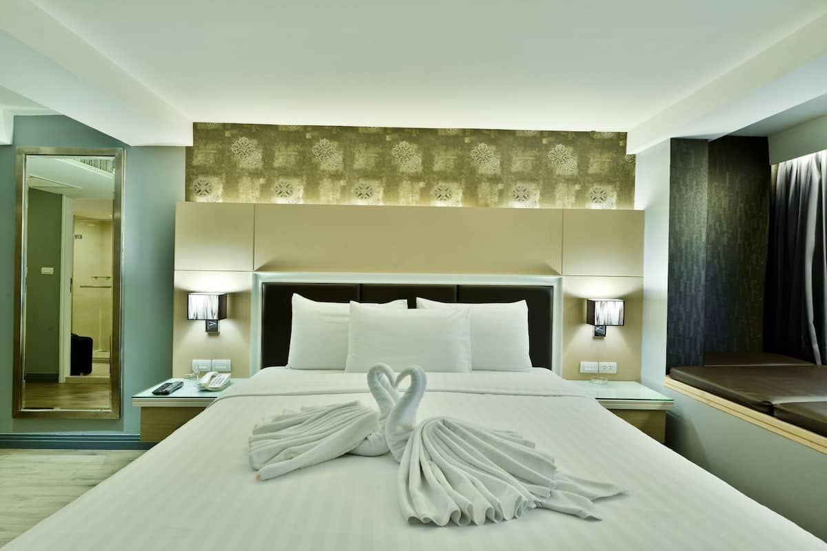 Habitación de hotel con cama, lámparas de noche, un espejo y una cama bien tendida con toallas.