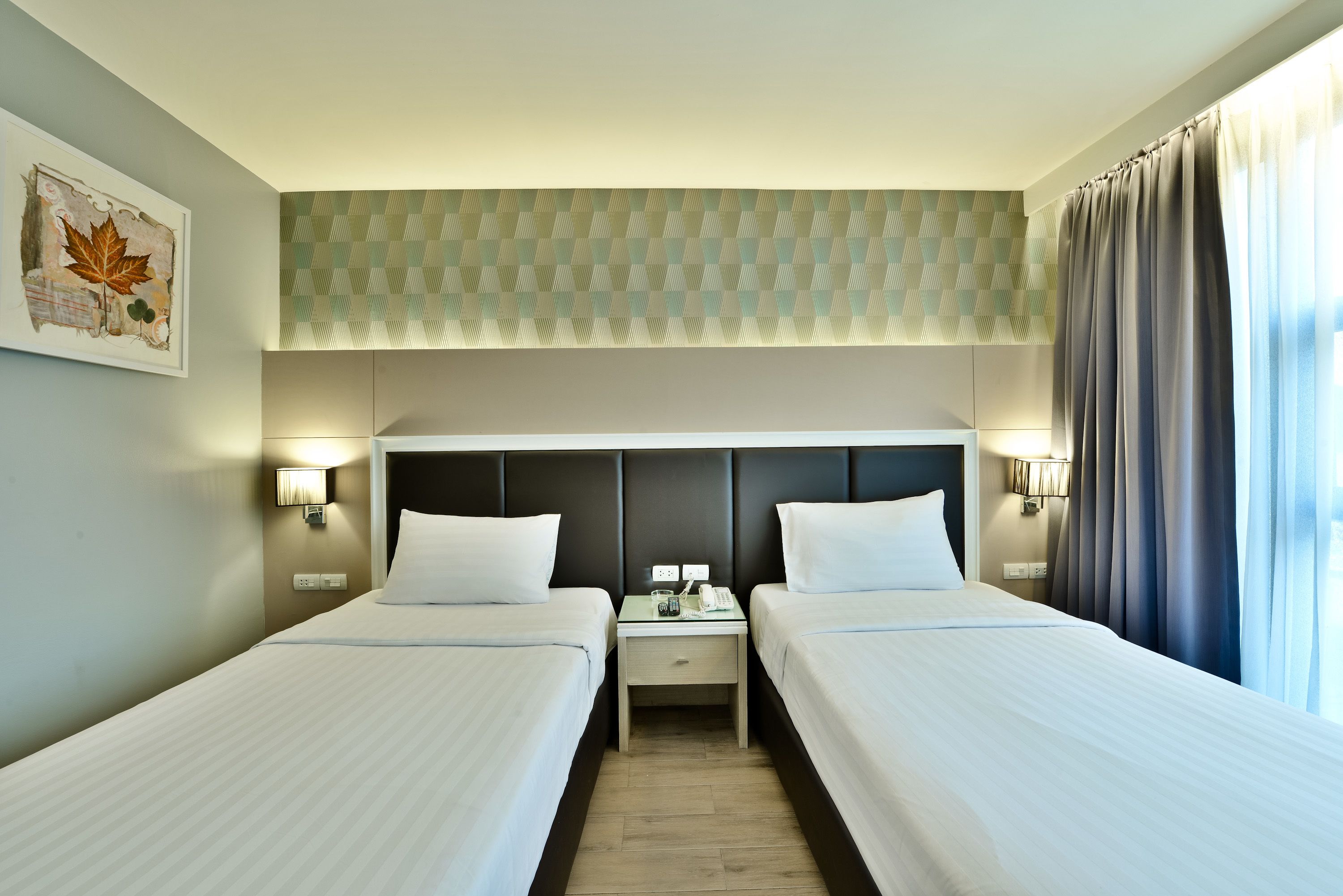 A hotel room with two beds, a headboard with a geometric pattern, bedside lamps, and a framed artwork on the wall.