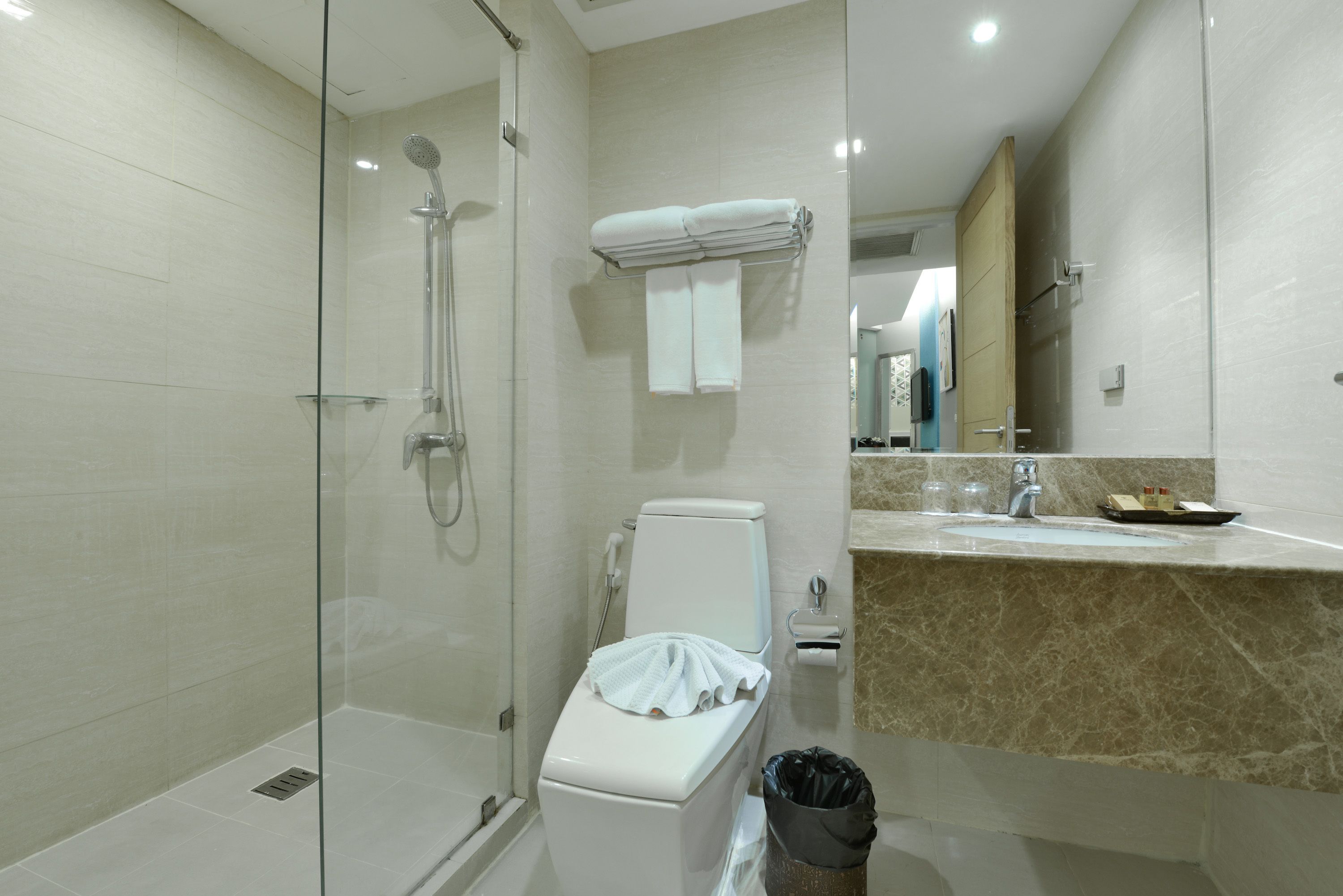 A modern bathroom with a glass-enclosed shower, a toilet with a towel rack, and a marble countertop with a sink and mirror.
