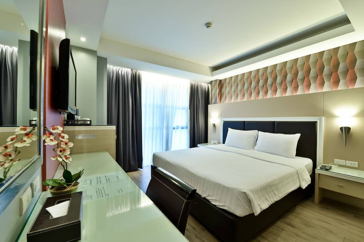 Una habitación de hotel moderna con una cama grande, un escritorio con computadora, un televisor y una ventana con cortinas.