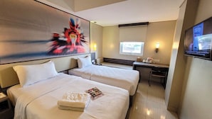 A hotel room with two beds, a desk, a TV, and a painting on the wall. - Cordela Kartika Dewi Jogjakarta (Yogyakarta)