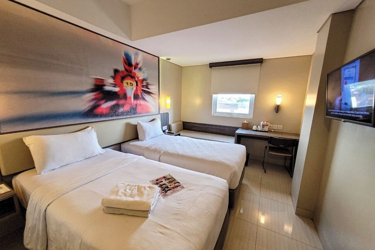 Une chambre d’hôtel avec deux lits, un bureau, une télévision et un tableau au mur.